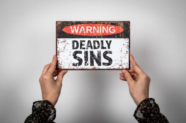 Ölümcül Günahlar. Beyaz arkaplan üzerindeki metin ile uyarı işareti.