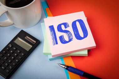 İSO. Ofis masasında metin, kahve fincanı, hesap makinesi ve kırtasiye malzemesi olan not defteri..