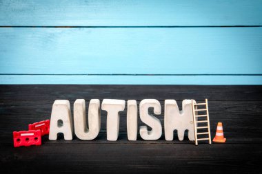 AUTİZM. Mavi ve siyah ahşap arka planda somut alfabe harfleri.