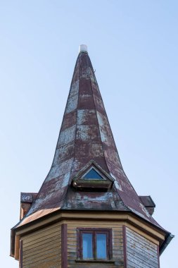Dik, yıpranmış konik çatısı ve küçük üçgen yatakhane penceresi olan eski ahşap bir kulenin yakın görüntüsü..