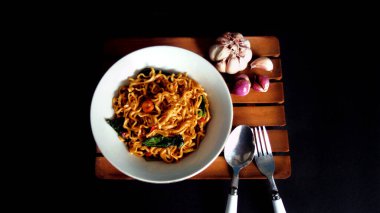 Beyaz kasede baharatlı erişte ve siyah arka planda sarımsak ve soğan. Ana yemek için lüks sebzeli Asya erişteleri servis edilir. Hazır yiyecek kavramının arka planı