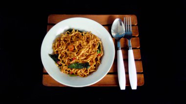 Siyah arka planlı, beyaz kaşık ve çatallı baharatlı erişte. Ana yemek için lüks sebzeli Asya erişteleri servis edilir. Hazır yiyecek kavramının arka planı