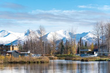 Spenard Gölü 'ndeki üsteki deniz uçakları, kar örtüsü Chugach Dağı ve Anchorage, Alaska' da sonbaharın başında hareketsiz kalan ağaçlar. Devlete ait yüzer uçak ve dünyanın en yoğun deniz uçağı üssü.