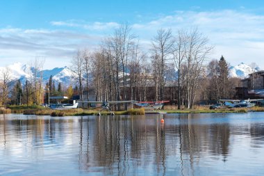 Spenard Gölü 'ndeki üsteki deniz uçakları, kar örtüsü Chugach Dağı ve Anchorage, Alaska' da sonbaharın başında hareketsiz kalan ağaçlar. Devlete ait yüzer uçak ve dünyanın en yoğun deniz uçağı üssü.