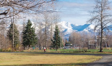 Arka planda deniz uçakları ve kar örtüsü Chugach Dağı ile Spenard Gölü yakınlarında çakıl patikası boyunca koşan beyaz elbiseli bir adam. Soğuk mevsimde sağlıklı, aktif, açık hava yaşam tarzı