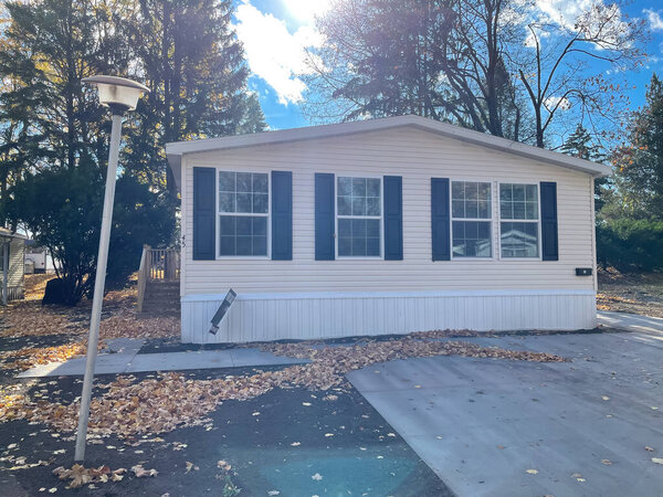Large concrete trowalk, parking space in front of brand new prefab mobile home with for sale yard sign post in Rochester, New York. Модульный дом с деревянной ступенью
