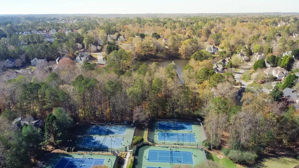 Upscale subdivision sprawl leading with tennis court complex, lakeside two story houses leading to horizontal line suburbs Atlanta, Georgia, USA. Aerial view recreational community sport facility