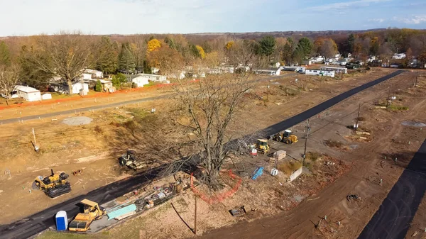 Aerial view heavy machines for foundation and earthmoving works at mobile home park construction site near row of completed manufactured trailer houses in Rochester. Upstate New York housing community