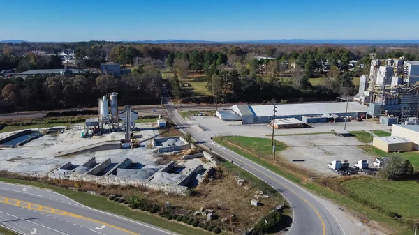Industrial zone with ready-mixed concrete batching plant, animal feed manufacturer near highway with Chestnut Mountain background in Georgia, USA. Aerial view cement silo, weigh hopper, conveyors
