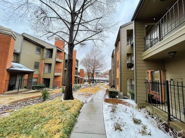 Rear view apartment building with patio balcony and concrete pathway in snow ice covered near Dallas, Texas, America after winter storm. Rental buildings townhome with shingle rooftop, cedar trees