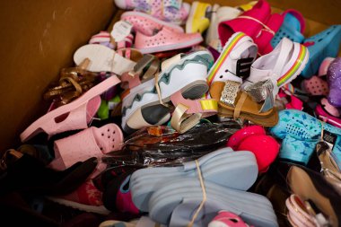 Mixed wide variety of brand new shoes tied in rubber band in large carton box at donation center in Dallas, Texas, USA. Collection drive footwear ready for volunteer activity