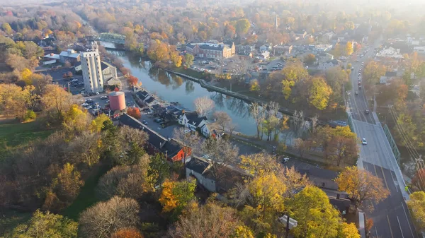Main Street and Erie Canal along riverside Pittsford town the oldest village in New York, USA with historic Schoen Place and colorful fall foliage. Aerial view suburb of Rochester autumn leaves