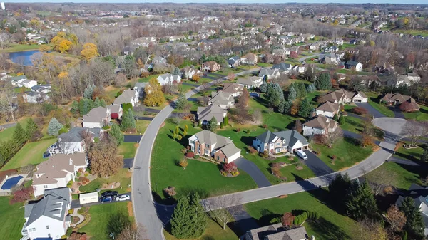 Master planned community low density housing design, row of two-story houses on grassy yards, no fence, colorful fall foliage to horizontal line Rochester, New York, USA. Aerial view upscale homes