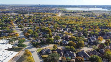Lakeside master planned community urban sprawl mixed of single-family homes and apartment complex, downtown building distance background colorful fall leaves in North Texas, USA. Aerial subdivision clipart