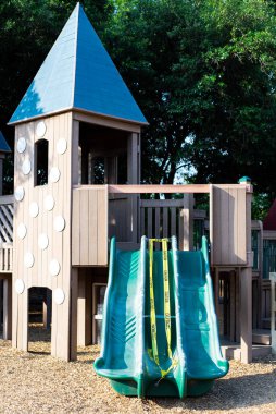 Tahta çocuk parkı, tepe örtüsü ve plastik üçlü kaydırak, Dallas, Teksas, ABD 'de inşaat sarı uyarı bant çim saman çim alanı altında. Halk parkındaki parlak sarı, koyu siyah metin tehlike bölgesi