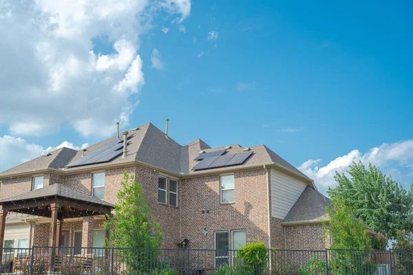 Black solar panels on shingle roofing of two story suburban residential house under sunny cloud blue sky in Flower Mound, Texas, America. Clean and renewable energy alternative power supply