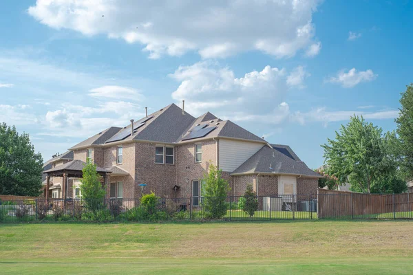 Two story suburban residential house with solar panel rooftop near rolling park side grassy lawn in Flower Mound, Texas, America. Clean and renewable energy alternative power supply