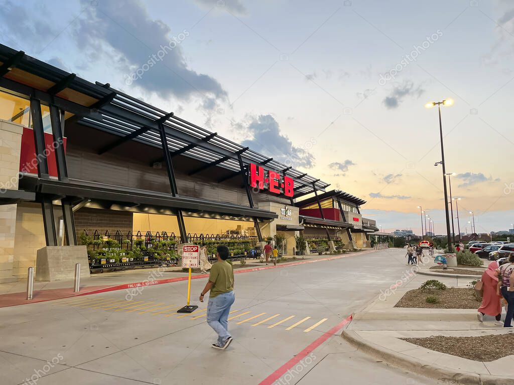 PLANO, TX, USA-JULY 8, 2023: Customer entering the facade entrance of recently opened H-E-B Grocery Company franchise supermarket chain with busy traffic at sunset. DFW Metroplex shopping location