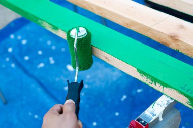 Asyalı bir adam Dallas, Teksas 'ta mavi muşamba kapaklı testere ile 2' ye 4 tahta tahtanın kenarına yeşil lateks boyayla boya yapmak için 15 santimlik boya silindiri kullanıyor. Ev yenileme projesi DIY