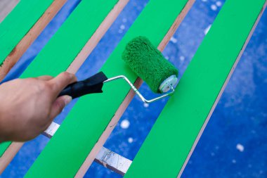 İkinci kat lateks boyası için 15 cm boyalı silindir kullanan Asyalı bir adam Dallas, Teksas 'ta mavi muşamba kaplı testere üzerinde 2' ye 4 tahta tahta yüzey kullanıyor. Ev yapımı DIY