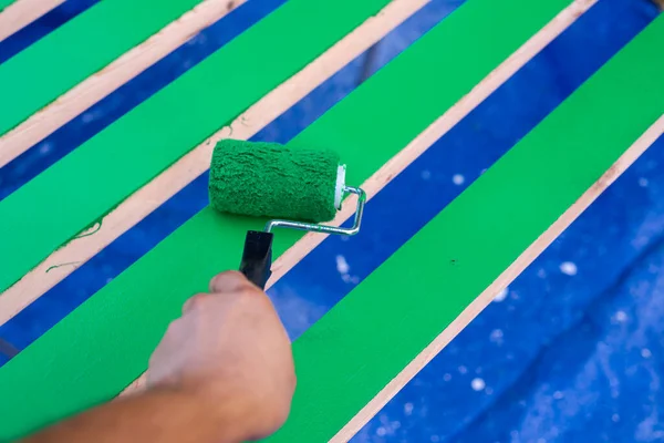 Left Asian man hand using 6 inches paint roller for second coat of latex paint smooth surface on 2 by 4 wooden boards on sawhorse with blue tarp cover drops in Dallas, Texas, USA. Home remodel DIY