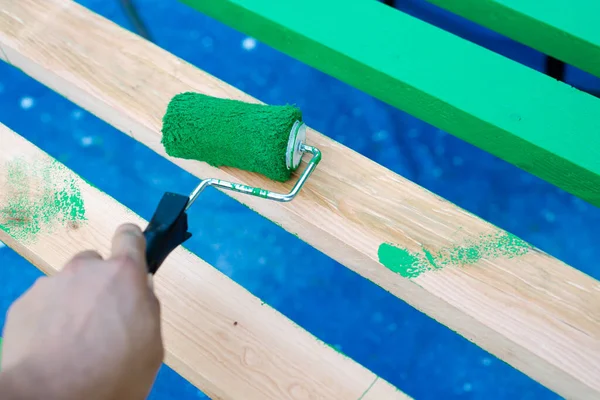 Hand using 6 inches paint roller for first coat of latex paint on 2 by 4 wooden boards on sawhorse with blue tarp cover paint drops outdoor in Dallas, Texas, USA. Home remodel renovation project DIY