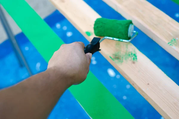 Hand using 6 inches paint roller for first coat of latex paint on 2 by 4 wooden boards on sawhorse with blue tarp cover paint drops outdoor in Dallas, Texas, USA. Home remodel renovation project DIY