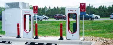 Robertsdale, AL, US-JUL 27, 2023: Benzin istasyonunun otoparkındaki Panorama Manzaralı Tesla Süperşarj İstasyonu, yüksek voltajlı DC doğrudan akım hızlı şarjlı ağ elektrikli otomobil üreticisi. Güneşli mavi gökyüzü