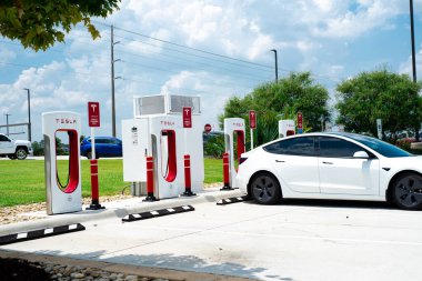 Robertsdale, AL, US-JUL 27, 2023: Tesla Model 3, büyük benzin istasyonu otoparkında sıcak yaz günü şarj ediliyor. Yüksek voltajlı doğrudan DC hızlı şarj şebekesi