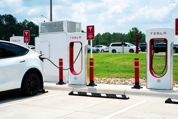 Robertsdale, AL, US-JUL 27, 2023: Tesla Model 3, büyük benzin istasyonu otoparkında sıcak yaz günü şarj ediliyor. Yüksek voltajlı doğrudan DC hızlı şarj şebekesi