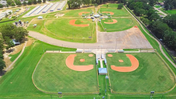 Community sport complex with multiple baseball, softball fields, batting cages, stadium seating, concession stand, playground near storage warehouse in Richland, Mississippi, USA. Aerial view park