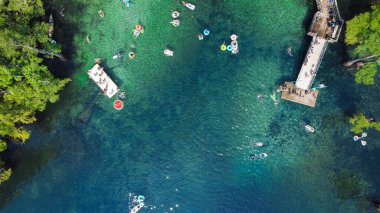 Şişirilebilir karpuz şamandırası, güverte atlaması, insanlar yüzmeyi, kanoya binmeyi, Walton County, Florida, ABD 'deki Morrison Springs County Parkı' nın turkuaz mavi suyunda dinlenmeyi seviyor. Gökyüzü yemyeşil kel selvi ağacı