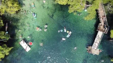 90 derecelik hava manzaralı güverteden atlayan insanlar Florida, Walton County 'deki Morrison Springs County Parkı' nın turkuaz büyüklüğünde mavi sularında yüzüyorlar.