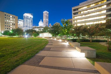 Houston şehir merkezi gökdeleni olan park meydanında aydınlık yol beton kaldırım akşam mavi saatinde arka planda başkent kulesi. Modern yüksek binalar, ofis binaları metro kompleksi ile işbirliği yapar