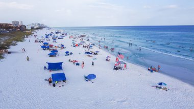 Miramar Sahili 'nin beyaz kumlu kıyı şeridi, turkuaz su, yüzen, rahatlatan, renkli çadırlar, tepe örtüsü ve yüksek katlı otel binaları, Destin, Florida. Seyahat hedefi