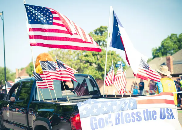 God bless the USA banner rear modern pickup truck dense of American flag on cargo bed driving on residential street smalltown Fourth of July parade, Dallas, Texas, USA blurry people. Independence Day