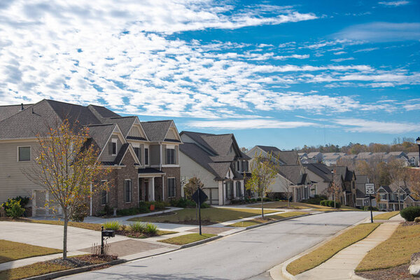 Residential street with speed limit leading down a steep hill row of two-story houses, new development subdivision neighborhood with upscale homes suburbs Atlanta, Georgia, USA. Sunny cloud blue sky