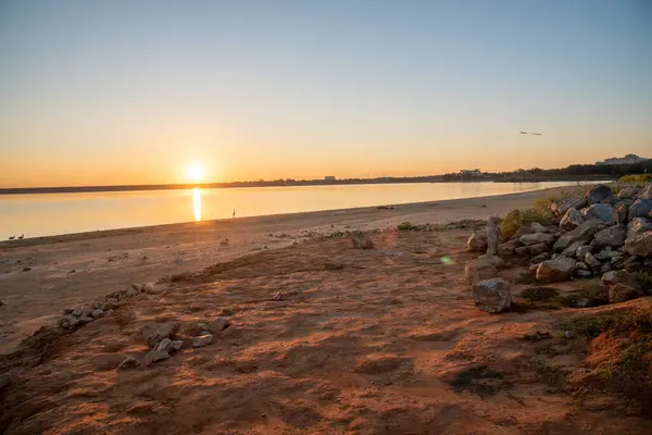 Sandy shoreline at beach area of Grapevine Lake with first appearance of light in the sky at dawn sunrise, rocky bank, fishing, camping activities, Flower Mound park. Scenery waterfront landscape