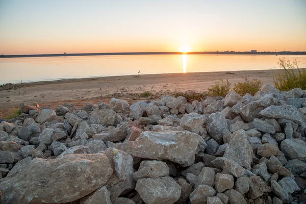Rocky bank of Grapevine Lake in Texas, USA with first appearance of light in the sky at dawn, sunrise, sandy shoreline, fishing, camping activities, recreation park. Scenery waterfront landscape