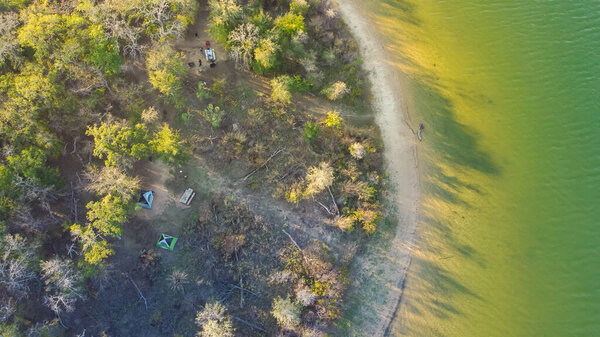 Curved shoreline and remote waterfront primitive camping sites with tents at Isle du Bois Ray Roberts Lake State Park lush green tree forest near Denton, Texas, US aerial view. Nature and adventurers