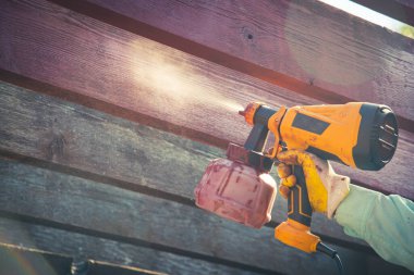 Adamın elinde tonlu fotoğraf lekesi tabancası ve eldivenli gömlek. Pergola ahşap dış yapıyı kızılağaç rengine boyuyor. Dallas, Teksas 'ta ev yenileme projesi. Kırmızı Sedir