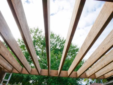 Yakın zamanda zımparalanmış pergola çatı kirişinin arka planında büyük bir ağaç var. Ağaç kirişlerini yeniden boyamaya hazır. Ağaç gövdeleri, Dallas, Teksas, ABD 'nin arka bahçe bahçesi, doğal ahşap tahıl. DYI