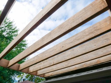 Yakın zamanda zımparalanmış pergola çatı kirişinin arka planında büyük bir ağaç var. Ağaç kirişlerini yeniden boyamaya hazır. Ağaç gövdeleri, Dallas, Teksas, ABD 'nin arka bahçe bahçesi, doğal ahşap tahıl. DYI