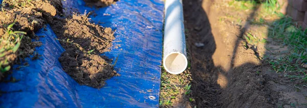 Panorama view plastic sewage pipes PVC, blue tarp with dirt, black mixing tub, pipe ready to laying, buried in ground trench, rainwater drainage residential house, Dallas, Texas, USA. Piping sewer
