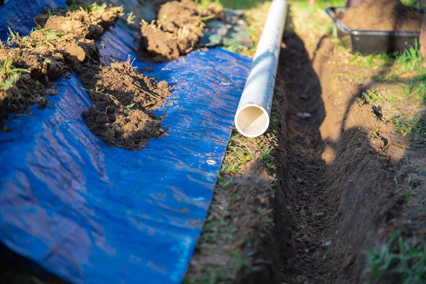 Selective focus plastic sewage pipes PVC, blue tarp with dirt, black mixing tub, pipe ready to laying, buried in ground trench, rainwater drainage residential house, Dallas, Texas, USA. Piping sewer