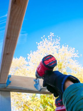 Kablosuz etki sürücüsünü kullanarak dış ahşap vidaları kiriş kiriş kiriş kirişinin altında askı desteği, gökyüzü düşüşü yeşillik arka planı, Teksas 'a iliştirin. ABD