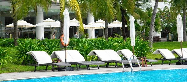 Panorama view upscale multistory resort hotel building with outdoor swimming pool, surrounding lush green coconut palm trees tropical garden, lounger chairs white cushion in Nha Trang, Vietnam. Travel