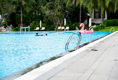 Vietnam 'daki lüks oteldeki büyük yüzme havuzunun doğrusal kanalizasyonları yakınındaki paslanmaz çelik korkuluklar, kılcal dalgalı temiz havuz suyu, açık hava eğlencesi. Boşluğu kopyala