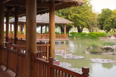 Su zambağı yüzen yapraklar minyatür kaya manzaralı gölet, beton sütun temelinde geleneksel Vietnam ahşap evleri, korkuluklar, palmiye yaprakları sazdan çatı, ayaklıklar üzerinde yükselen. Asya