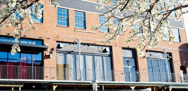 Historic multistory brick building with blossom Bradford Pear tree along canal river walk at Bricktown entertainment district, travel destination attractions in Oklahoma, sunny clear blue sky. USA clipart